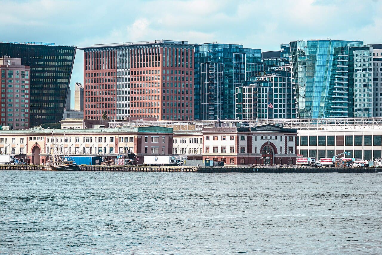 The low brick buildings of the Boston Fish Pier seen across the harbor, with Seaport office towers behind them