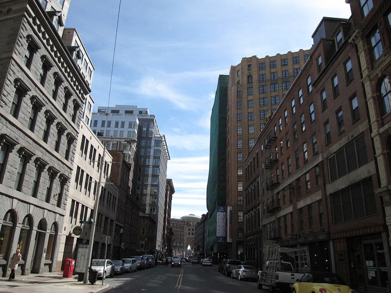 Broad Street in Boston's Financial District lined with granite and brick buildings, with the Rowes Wharf arch at the far end