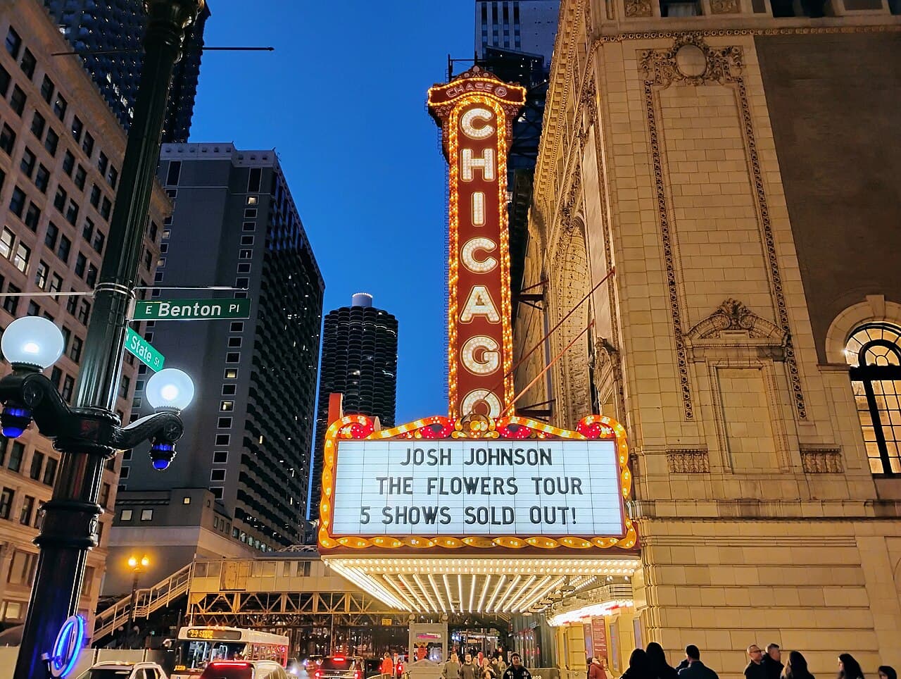 The lit CHICAGO sign and marquee of the Chicago Theatre on State Street at dusk, with the elevated 'L' tracks and a Marina City tower behind