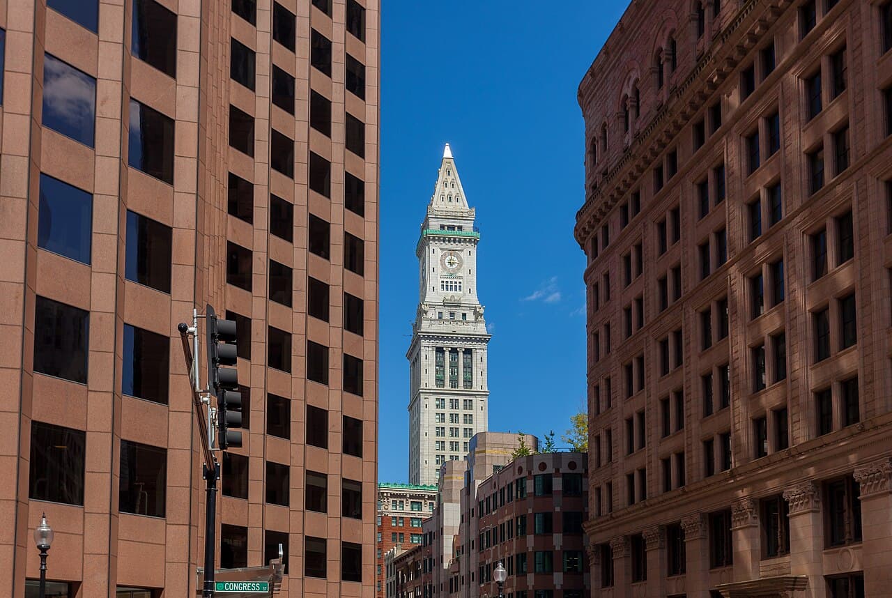 The Custom House Tower's white clock tower framed by office buildings at Congress Street in Boston's Financial District, under a blue sky
