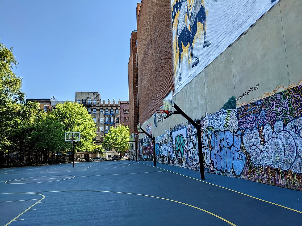 Empty outdoor pickup basketball courts with graffiti murals on the wall at the Lower East Side Playground in the East Village