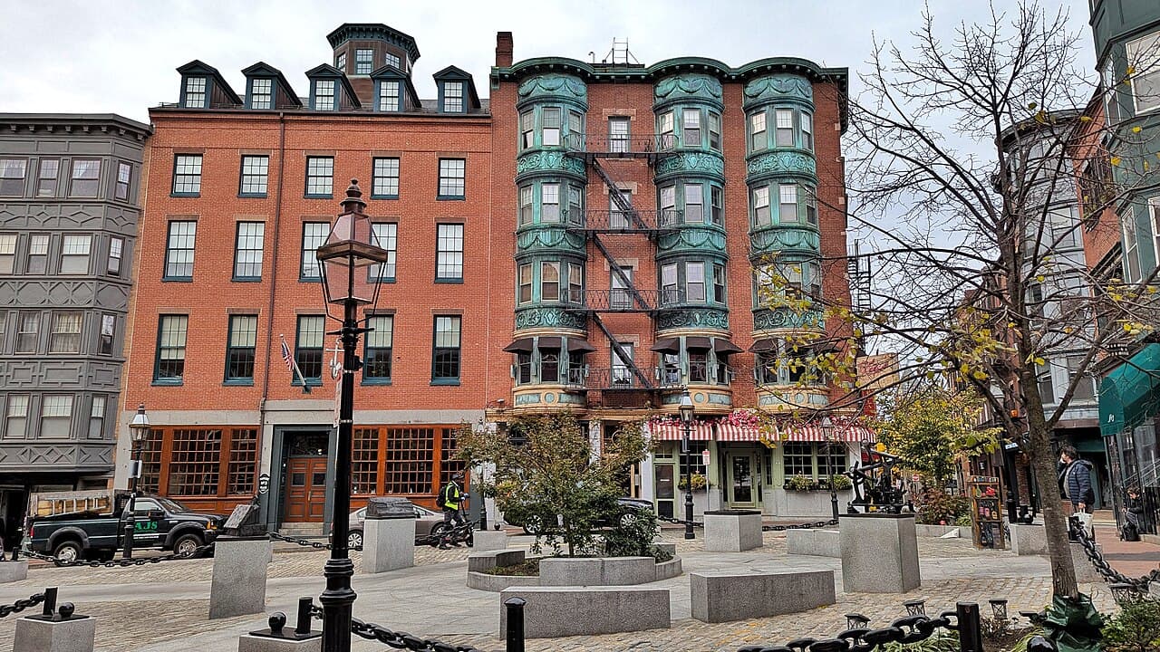 The cobbled plaza of North Square in Boston's North End, with brick buildings, lamp posts and granite benches