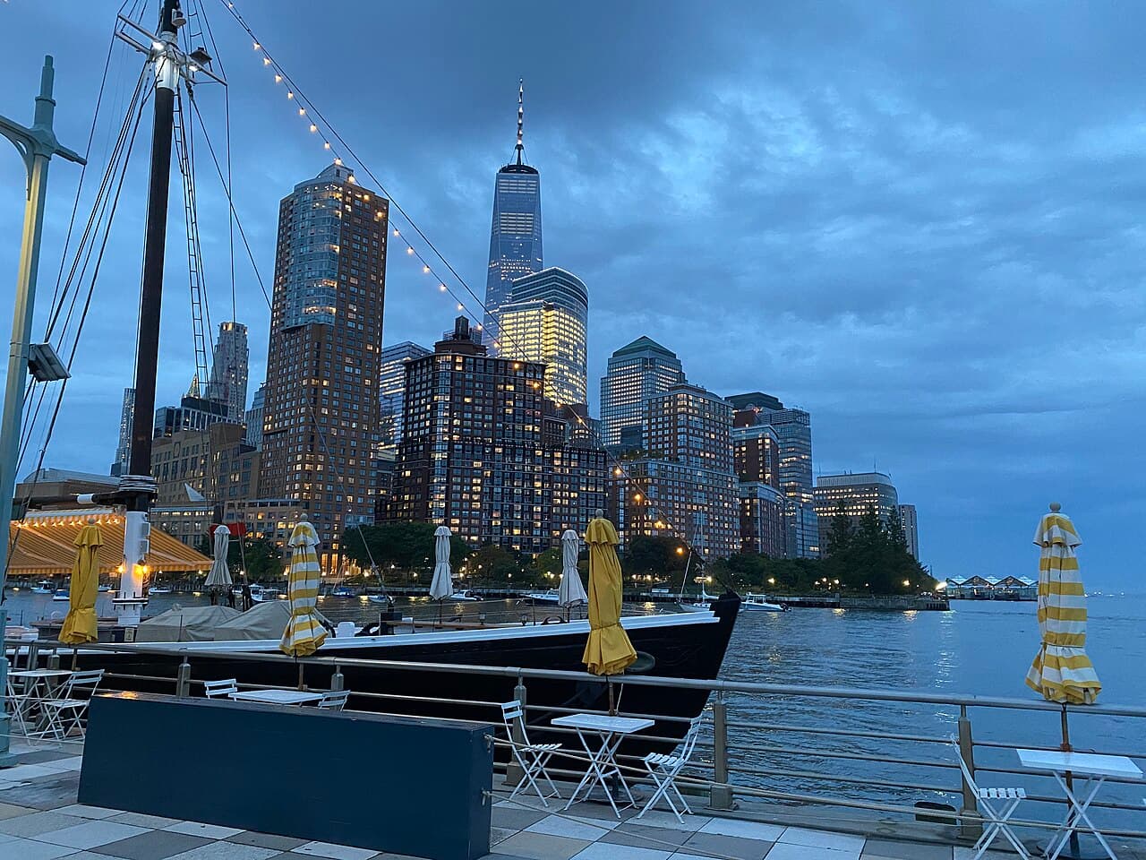 Pier 25 in Hudson River Park at dusk, with tables by the water and the Lower Manhattan skyline behind