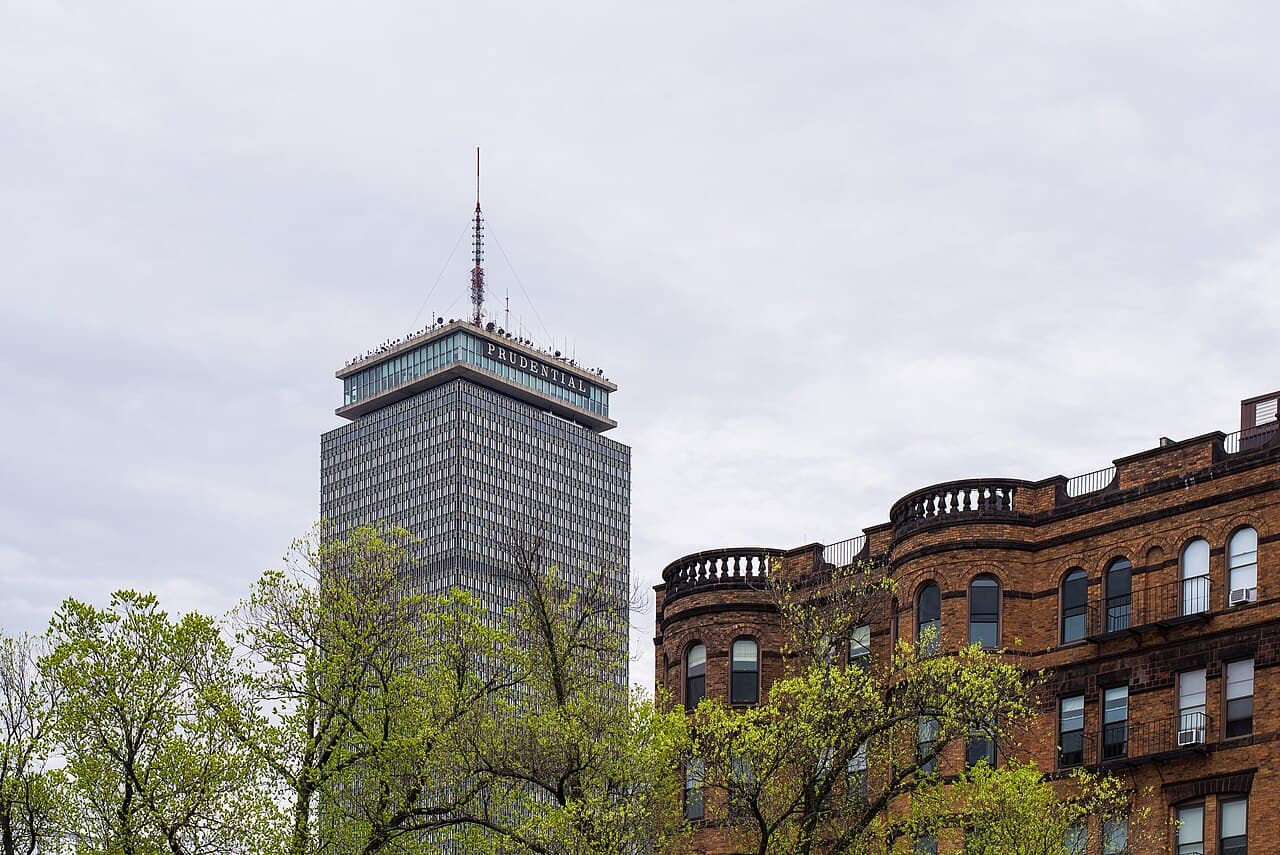 The Prudential Tower rising behind spring trees and a curved brownstone building in Back Bay, Boston