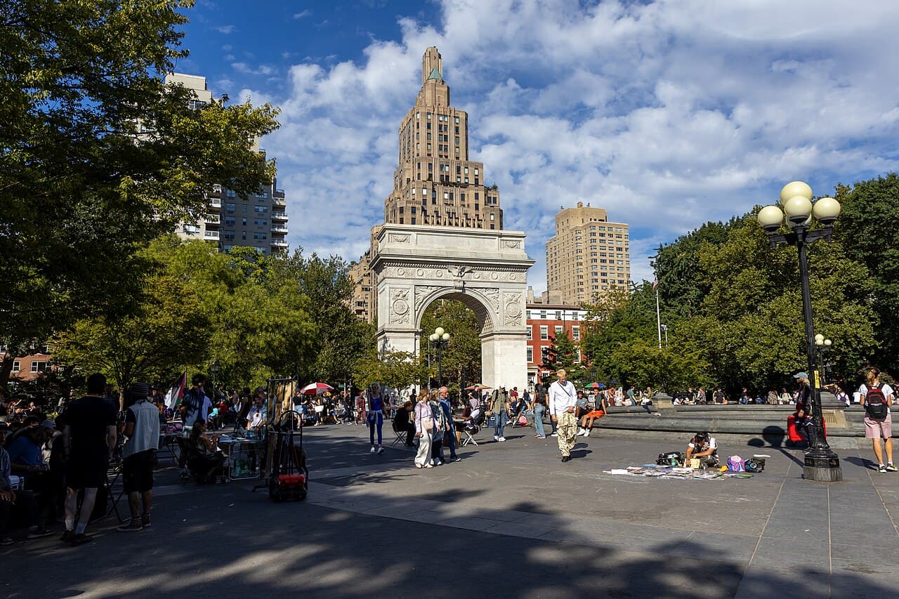 People walking through Washington Square Park toward its arch on a sunny day in Greenwich Village