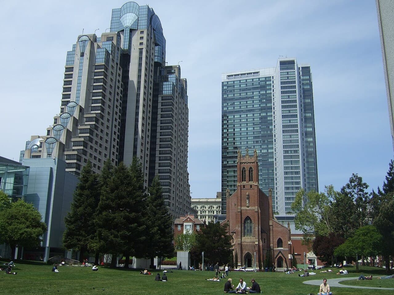 People sitting on the lawn of Yerba Buena Gardens, with St. Patrick Church and downtown towers behind it