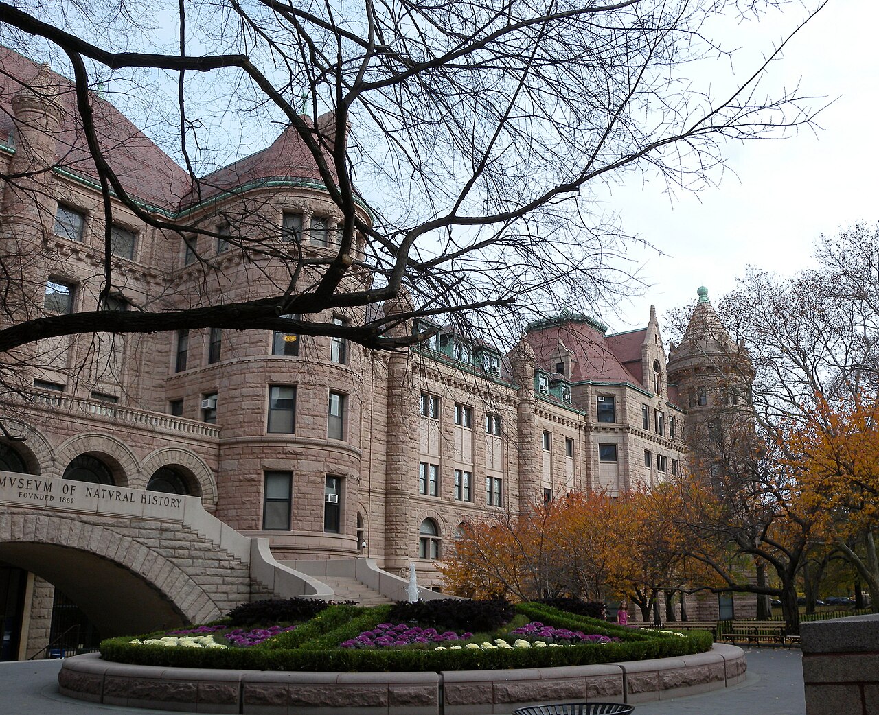 The red stone south front of the American Museum of Natural History on West 77th Street, with a flowerbed and autumn trees