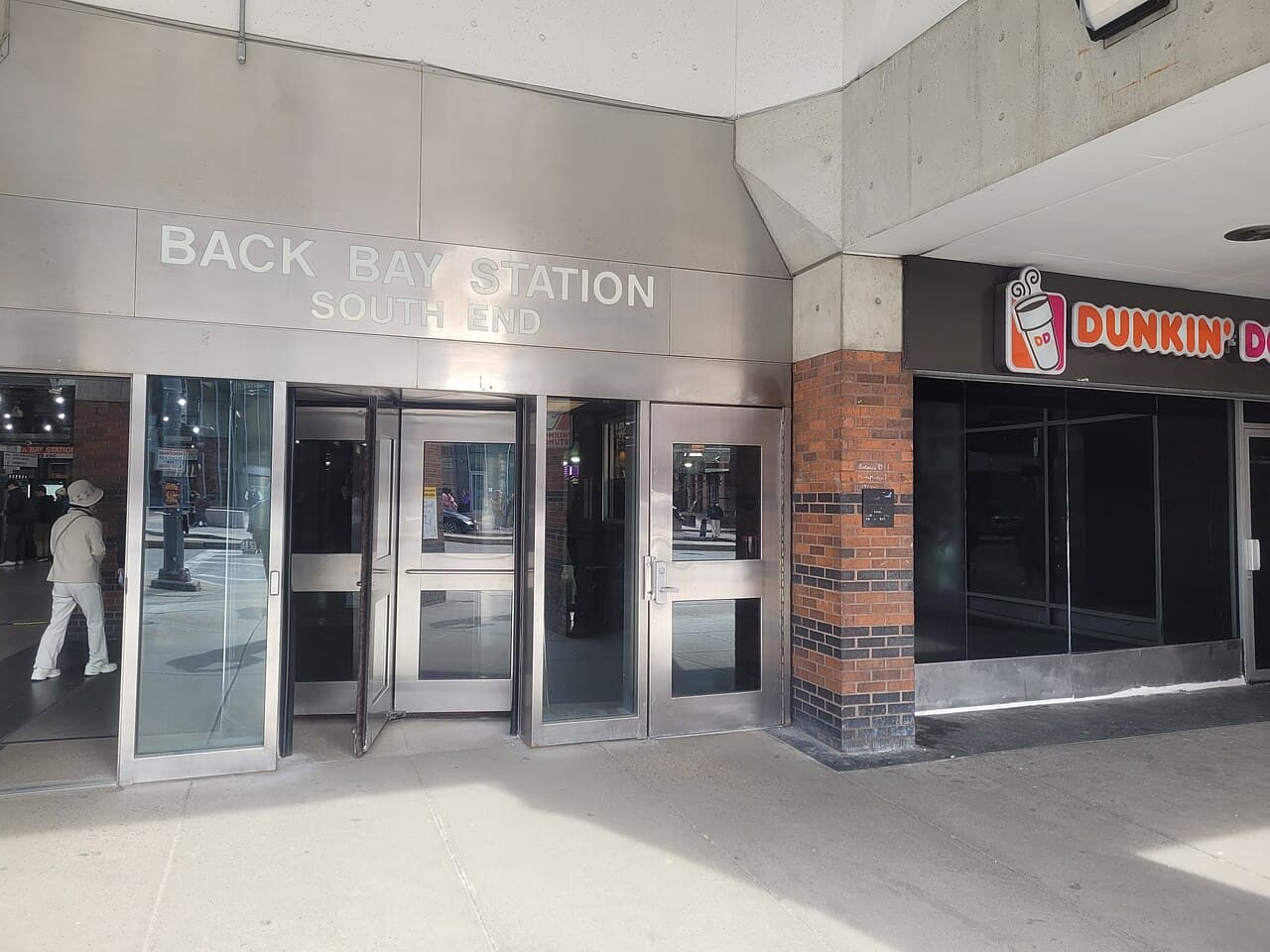 The steel and glass doors of the Back Bay station entrance on Dartmouth Street in Boston, under a sign reading Back Bay Station South End