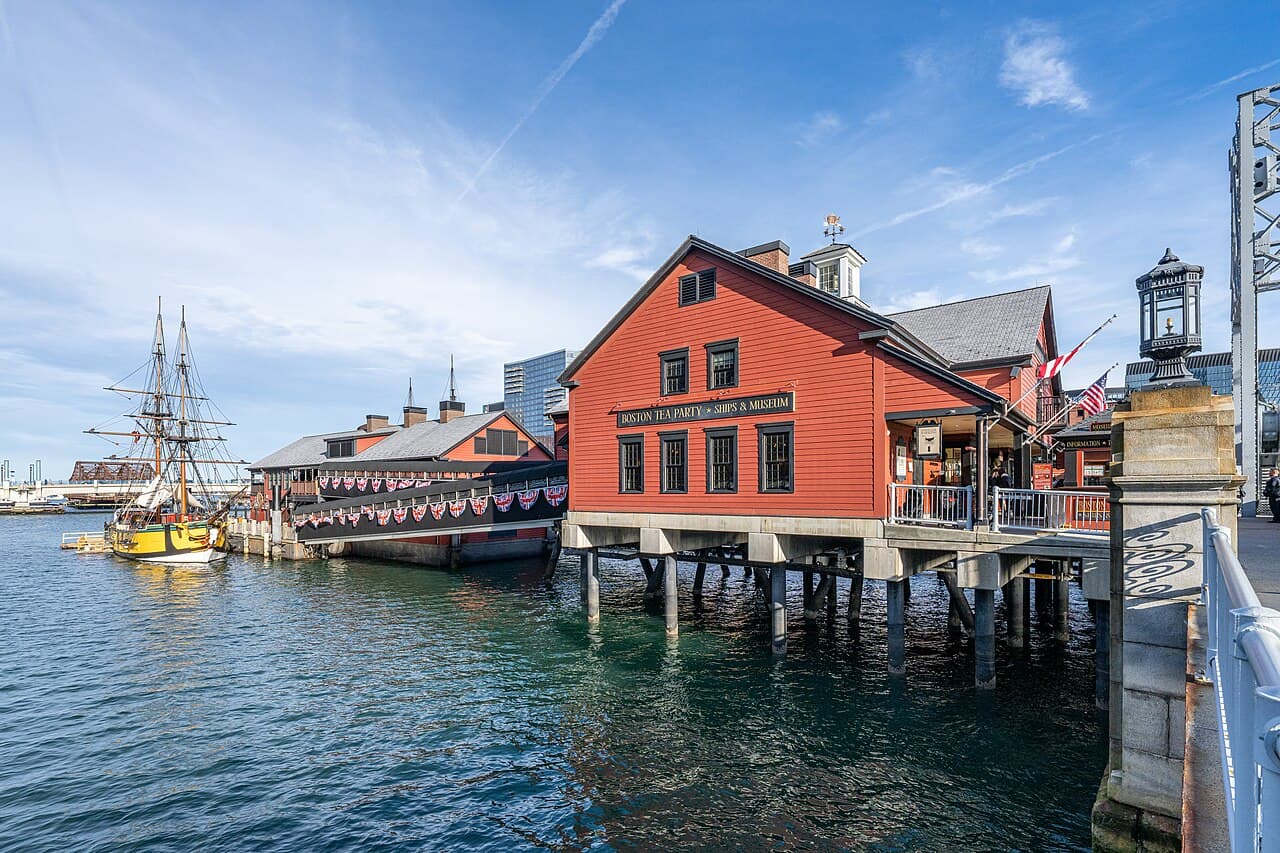 The red wooden Boston Tea Party Ships and Museum building on pilings over Fort Point Channel, with a tall ship docked beside it