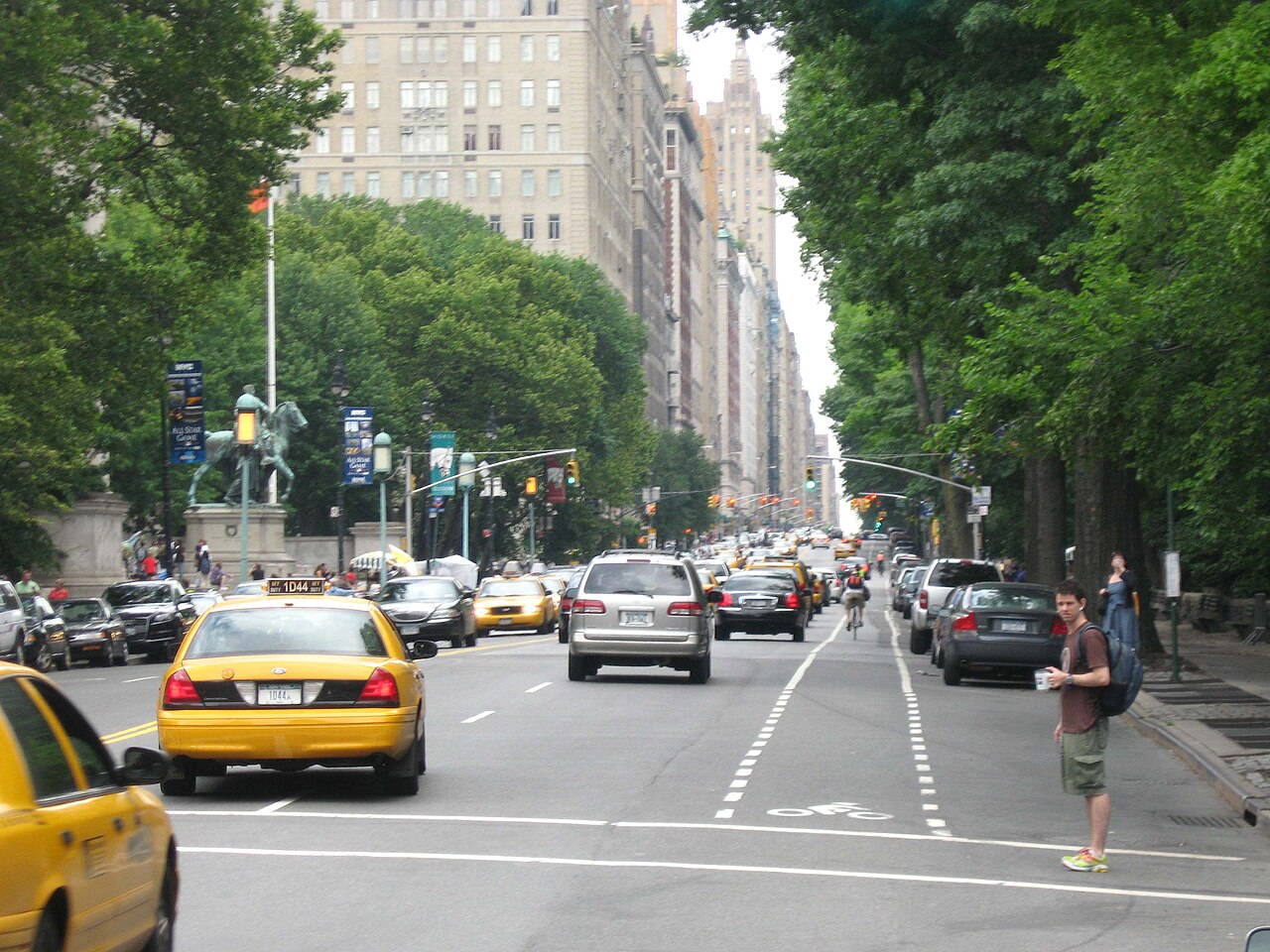 Taxis and cars on Central Park West looking north past the natural history museum, with Central Park's trees on the right