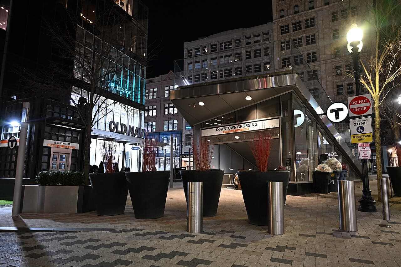 The glass entrance to the Downtown Crossing station on Franklin Street in Boston at night, with planters in front of it