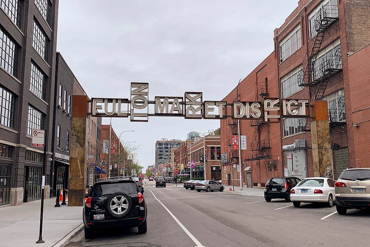 The Fulton Market District sign arching over a street of brick warehouse buildings in Chicago's West Loop