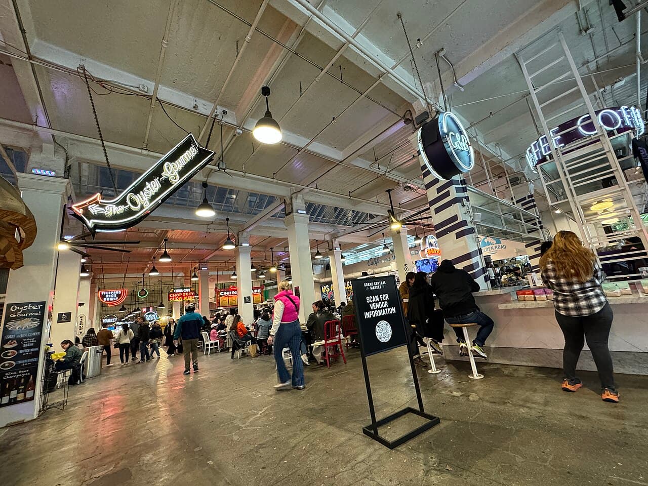 People walking past food stalls and neon signs inside Grand Central Market in Downtown LA