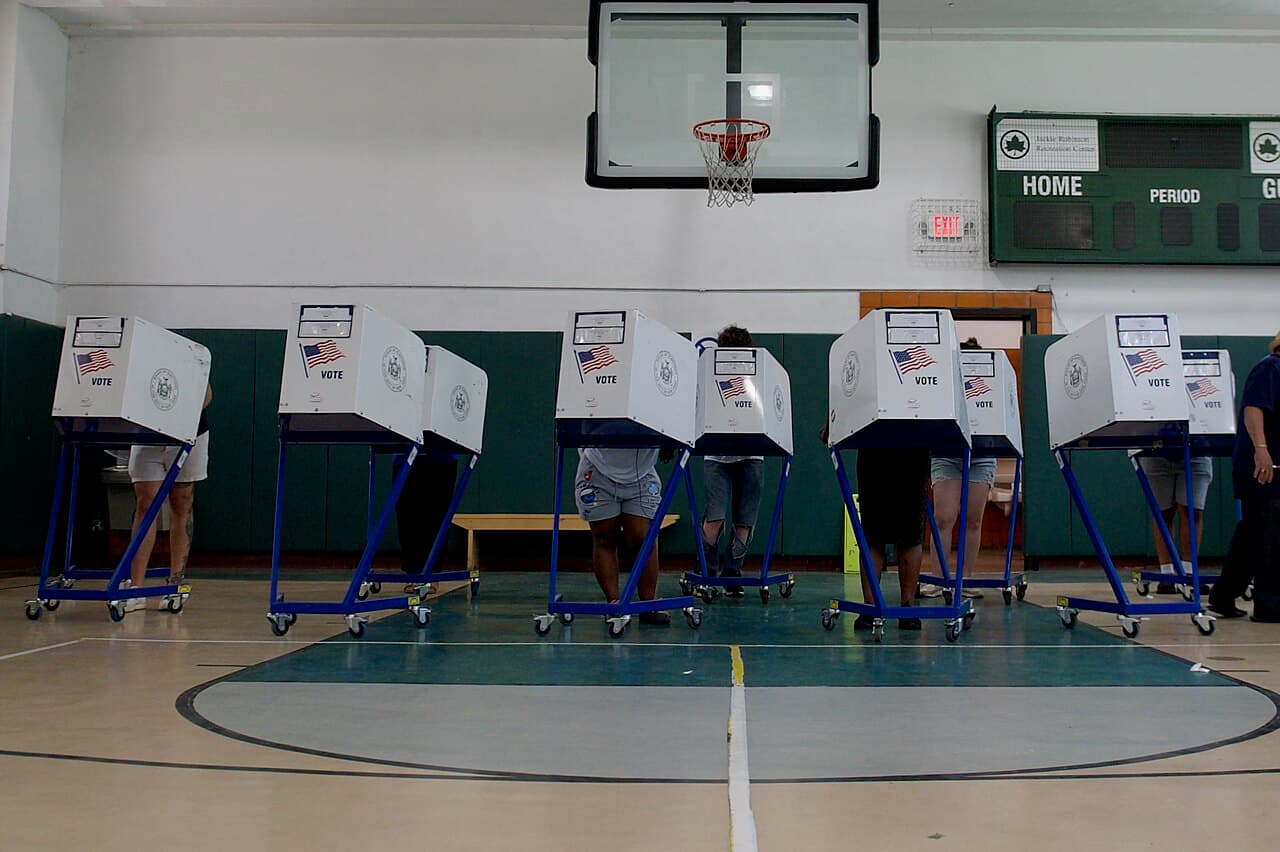 Voting booths set up on the indoor basketball court at the Jackie Robinson Recreation Center in Harlem, under a hoop and scoreboard