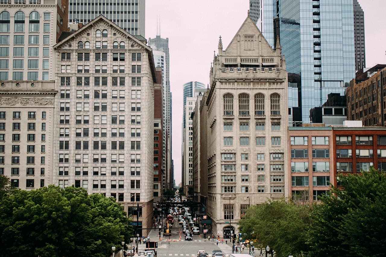 Historic stone buildings and glass towers across Michigan Avenue, seen from the trees of Millennium Park in the Chicago Loop