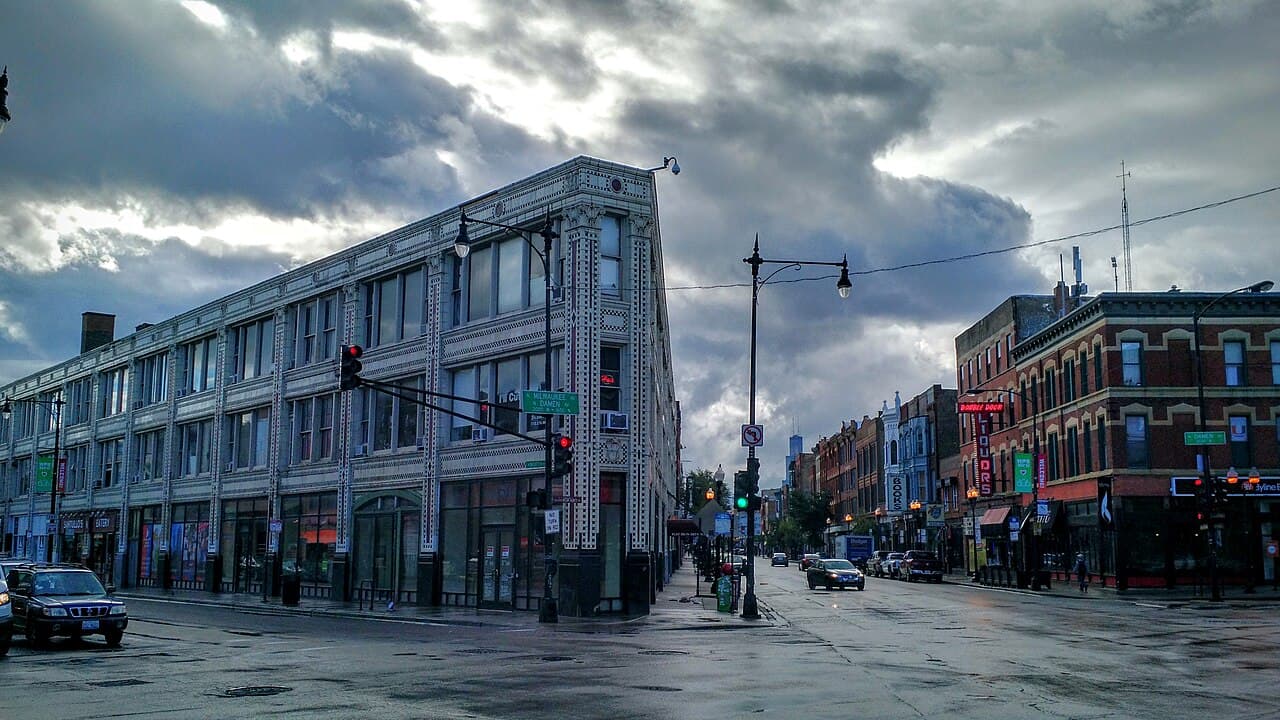 A white terra cotta building and older brick storefronts at the corner of Milwaukee and Damen avenues in Wicker Park under a cloudy sky