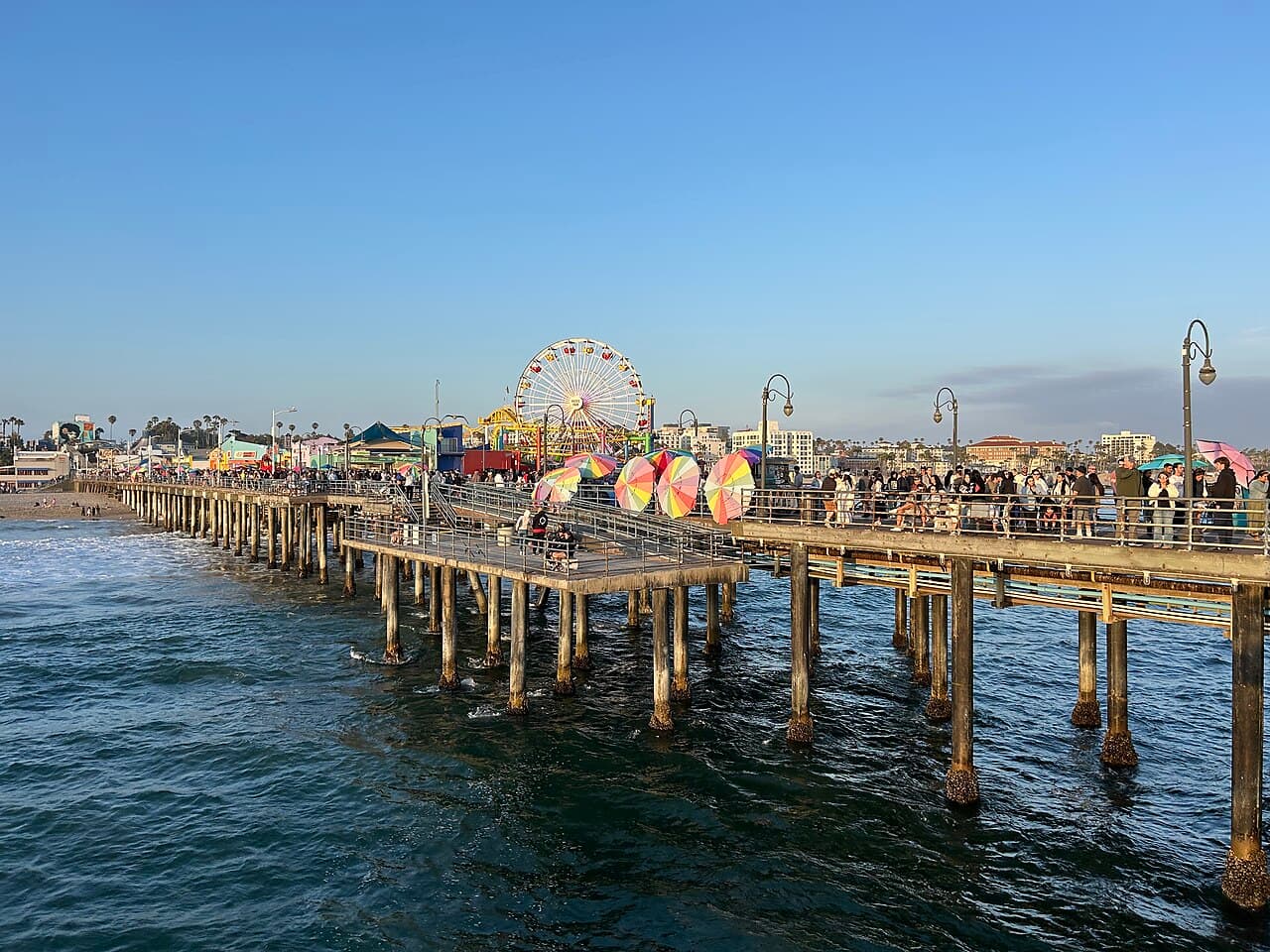 The Santa Monica Pier over the Pacific Ocean at sunset, with its Ferris wheel and a crowd along the rail