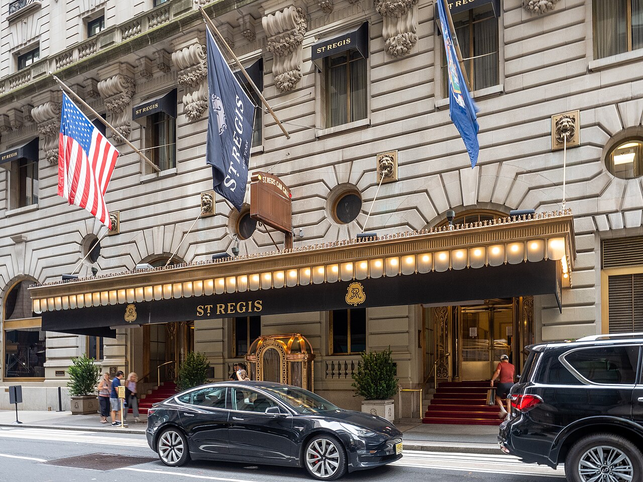The St. Regis New York's entrance on East 55th Street, with flags above a lit gold canopy and red-carpeted steps