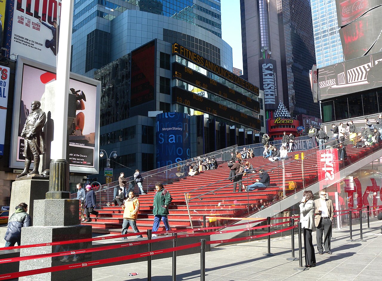 People sitting on the red steps above the TKTS booth in Times Square on a sunny day