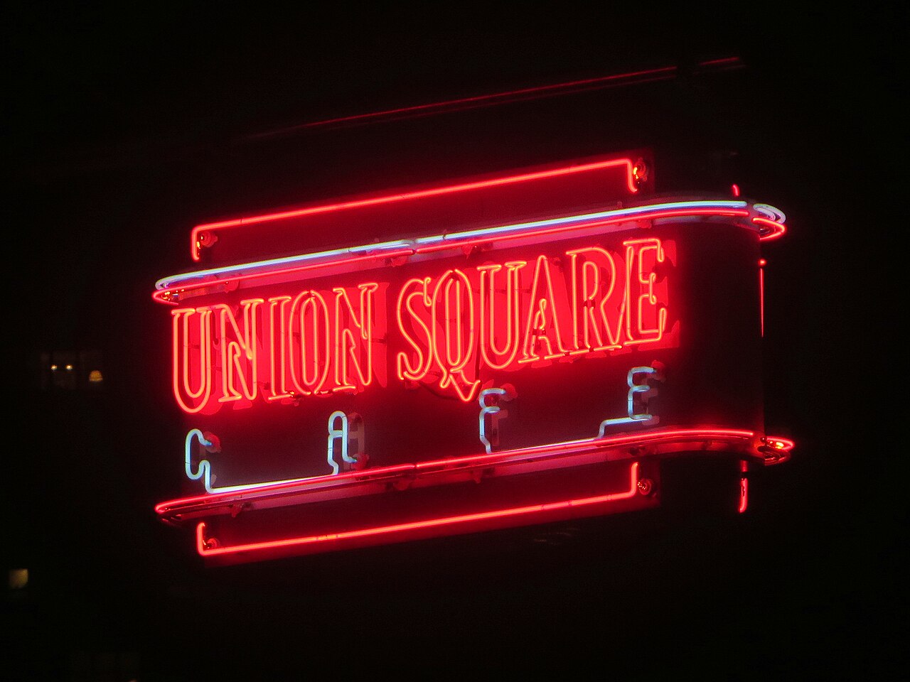 The red and white neon sign of Union Square Cafe glowing at night