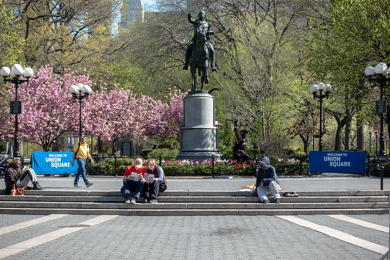 People sitting on the steps below the George Washington statue at the south end of Union Square Park in spring